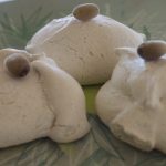 Three white meringues sit on a pale green plate. They have a small berry balanced on top.