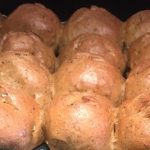 A tray holds glossy brown bread rolls flecked with wattleseed